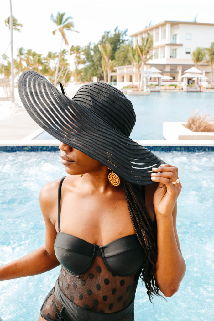 black polka dot swimsuit, black floppy hat, infinity pool, luxe vacation