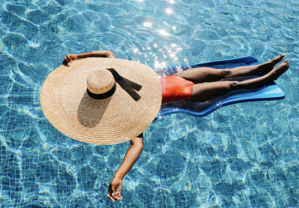 woman floating at the pool with an oversized straw sun hat for the summer