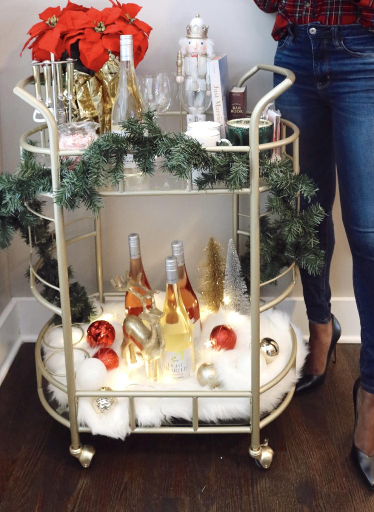 woman showing how to style holiday bar cart with decorations, glasses, and wine