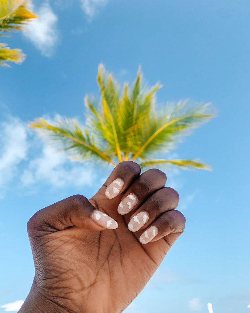 woman showing her painted nails against the sky and palm tree