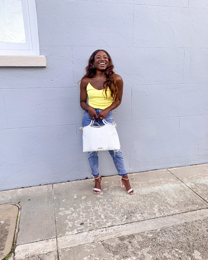 woman smiling and wearing yellow top and denim jeans
