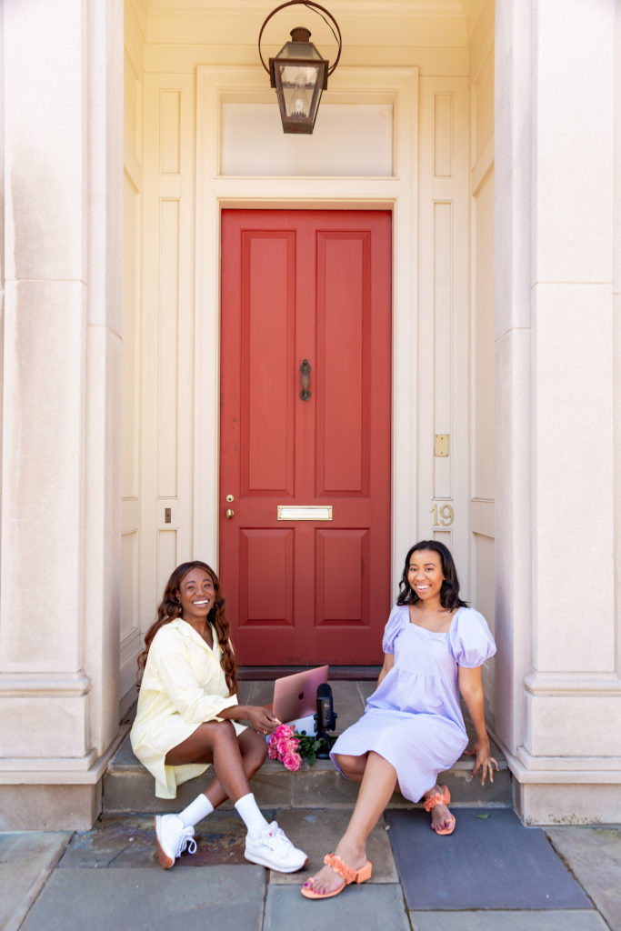two women sitting down outside a red door for culture podcast