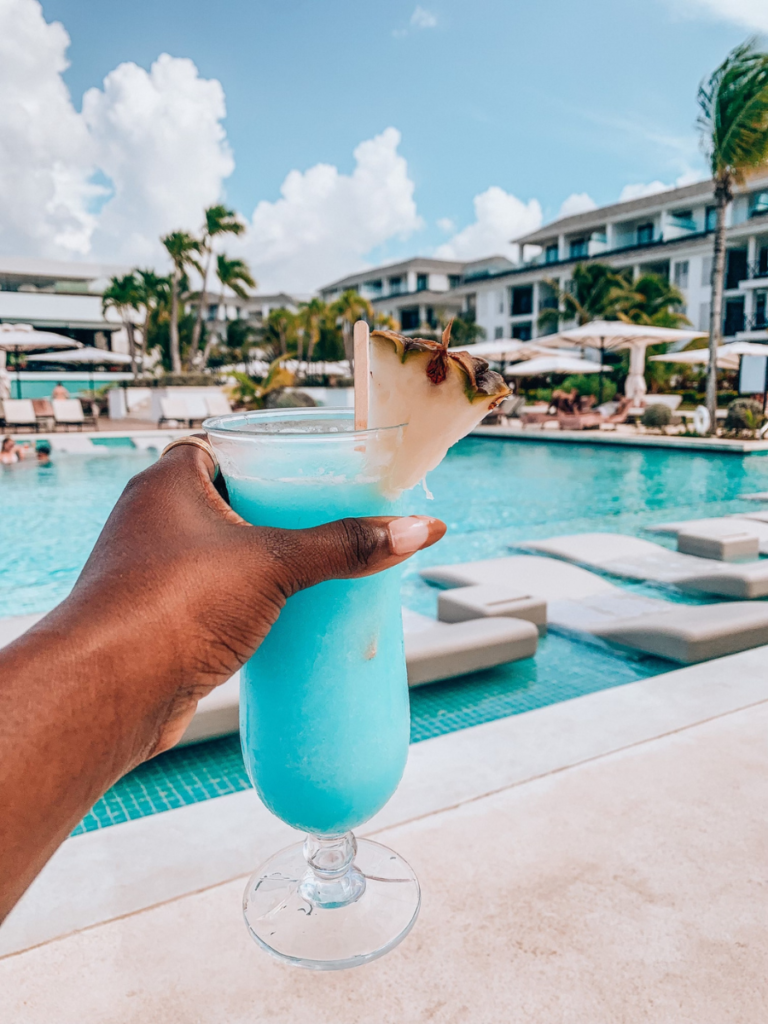 woman holding blue cocktail with pineapple garnishing in front of pool