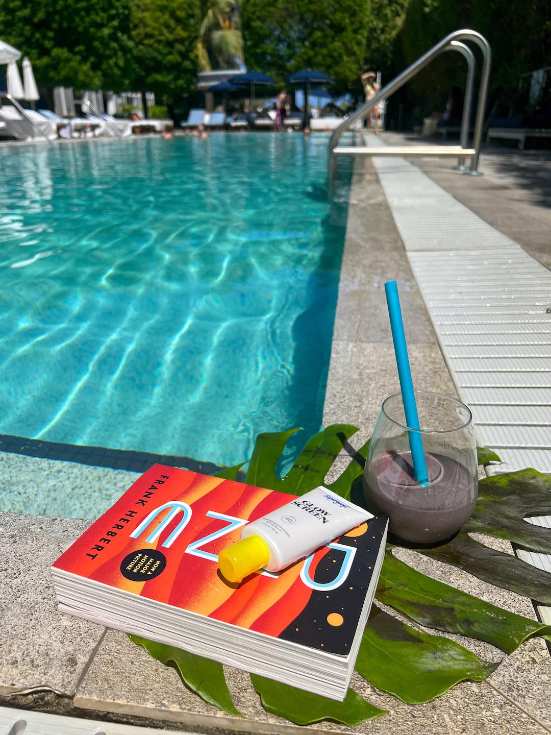 Poolside picture of smoothie, sunscreen and a book