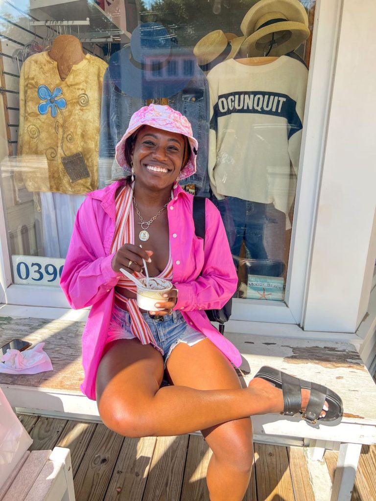 goodtomicha posting in pink bucket hat, pink button down and denim shorts