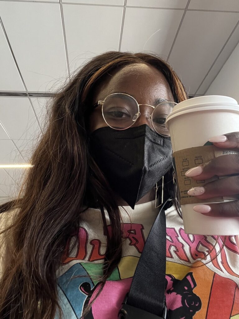 goodtomicha on an airplane in a mask holding coffee